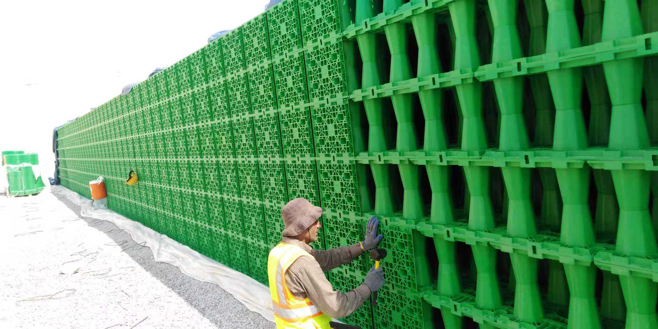 Trabajador ensamblando la pared lateral de un tanque modular verde de detención de aguas pluviales